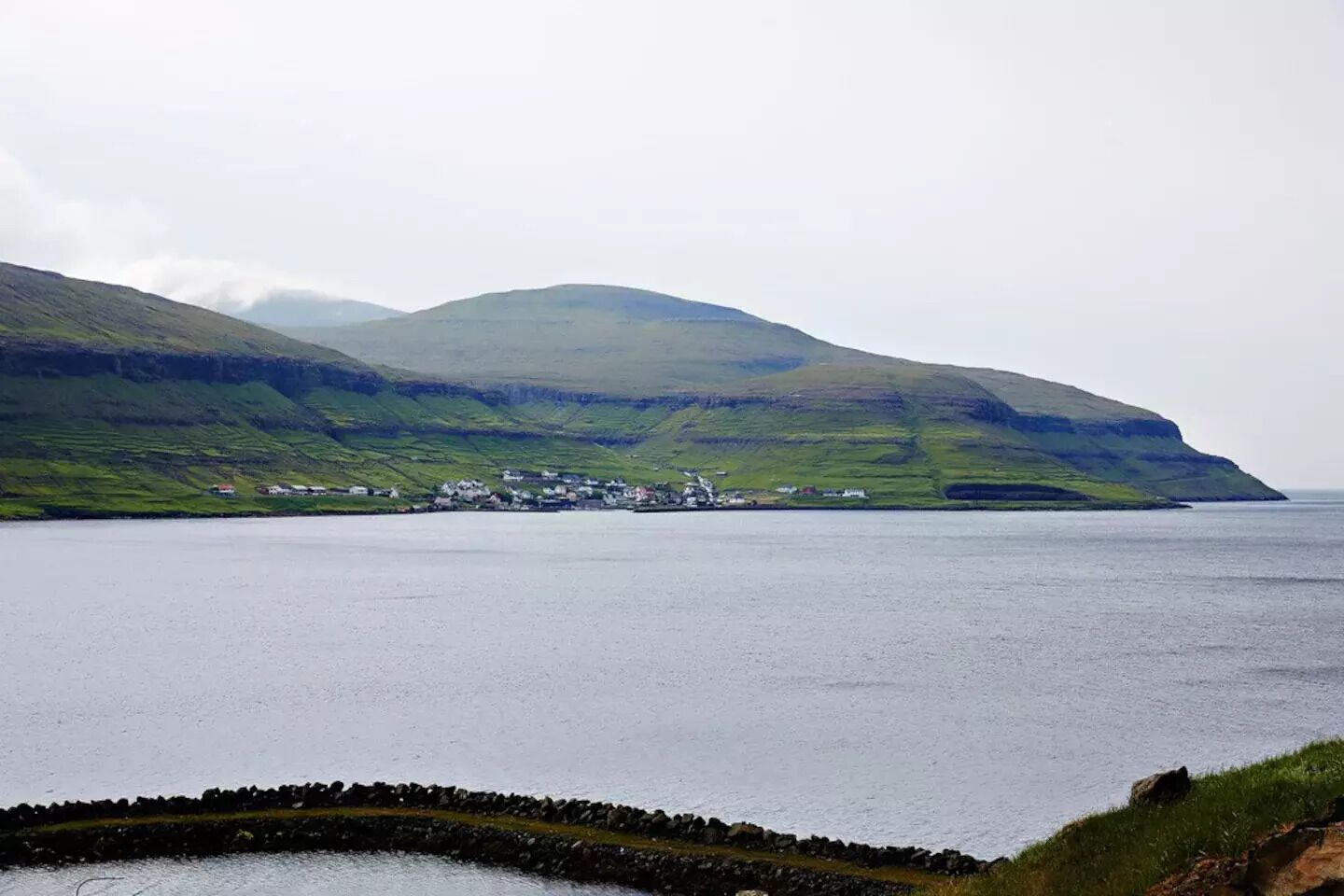 Un paysage côtier avec un petit village perché sur une colline, une côte rocheuse et une mer calme.