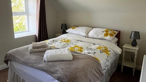 Una cama bien hecha con ropa de cama floral, dos lámparas de noche y una ventana con cortinas.