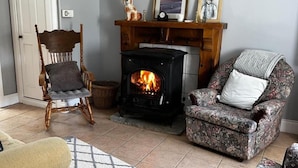 Una sala acogedora con chimenea, una silla de madera, un sillón estampado y una alfombra.