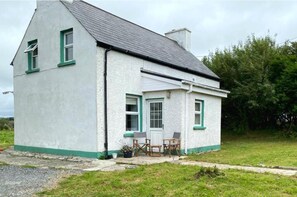 A single-story house with a gabled roof, a front porch with chairs, and a small garden area. - 3br-sea View-fireplace-garden-free Parking (Falcarragh)