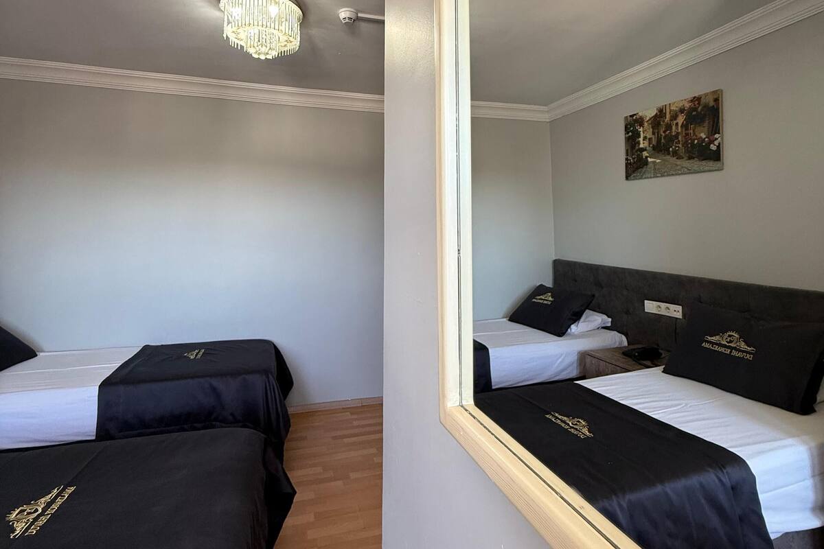 A hotel room with two beds, a chandelier, a painting on the wall, and a mirror reflecting the room.