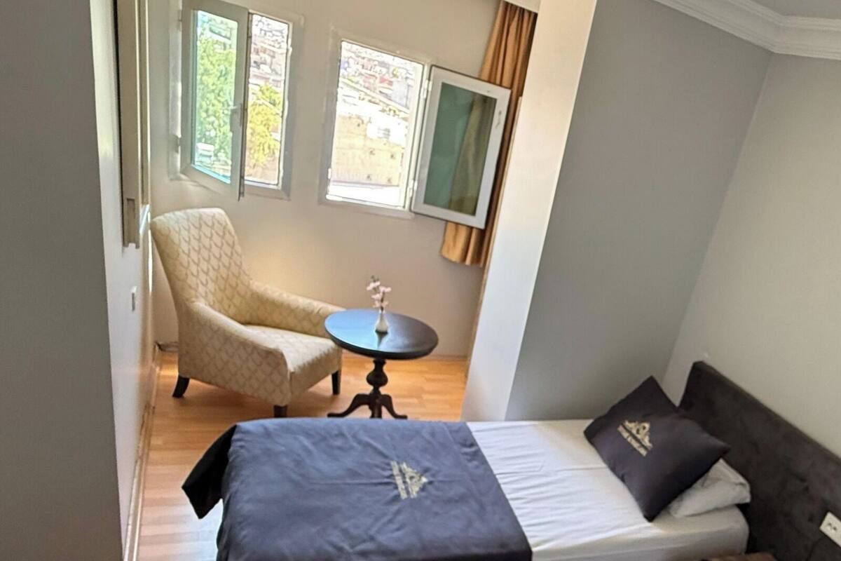 A bedroom with a bed, a chair, a small table, and a window.
