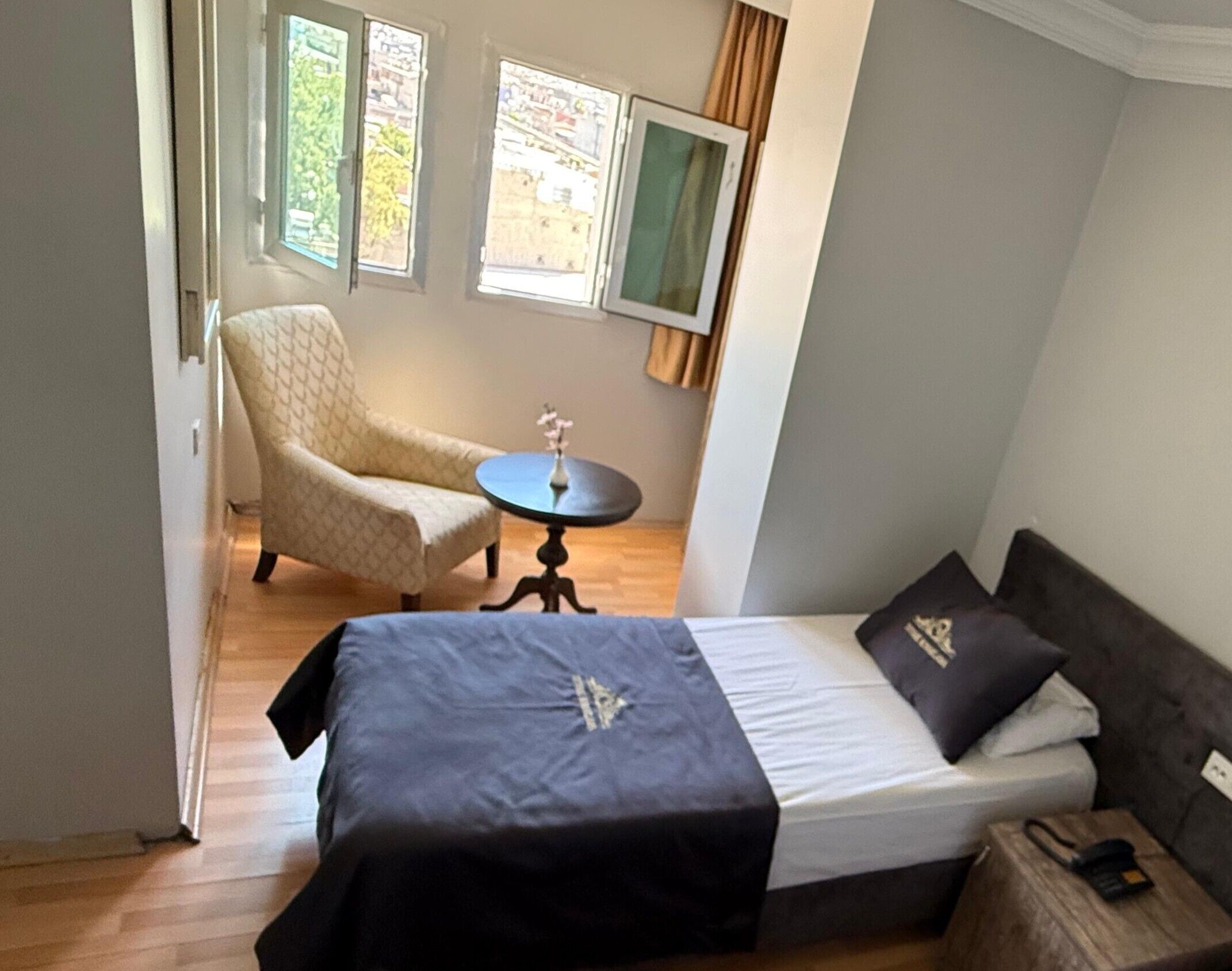 A bedroom with a bed, a chair, a small table, and two windows.