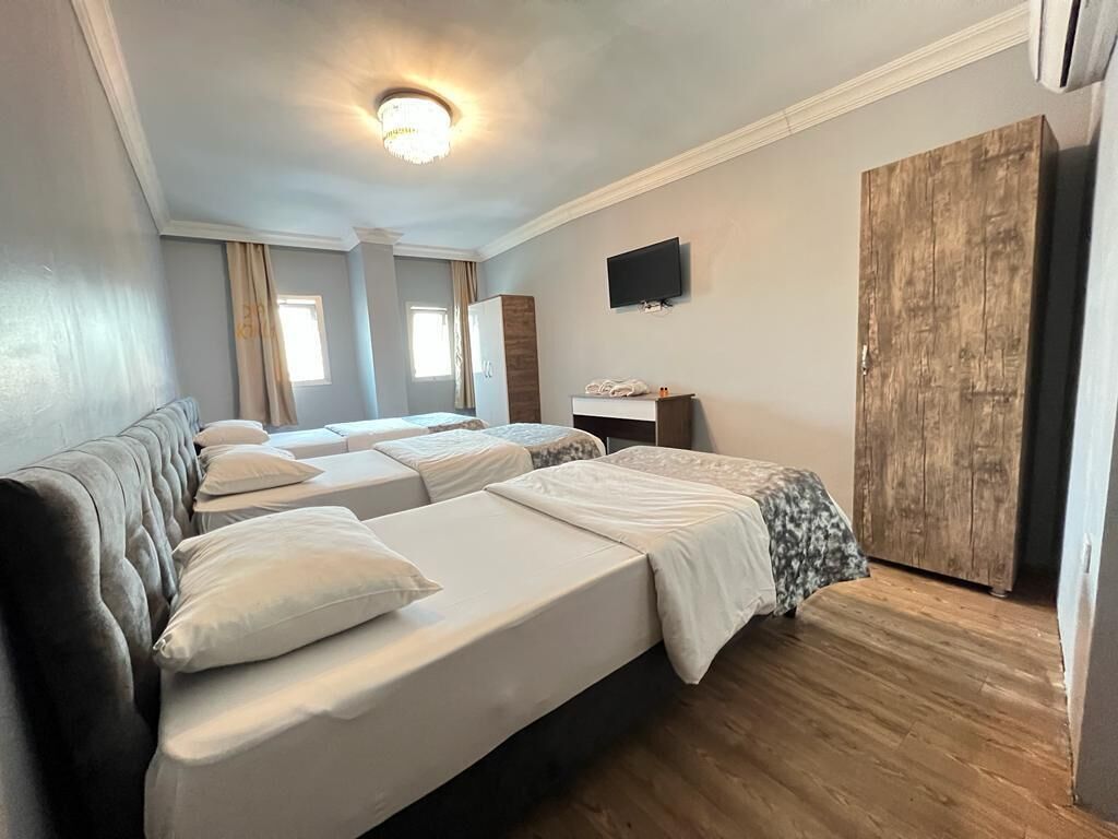 A hotel room with three beds, a television, a wooden wardrobe, and a ceiling light.