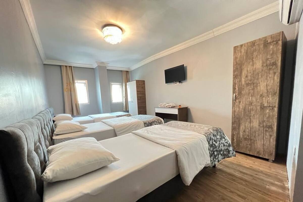 A hotel room with three beds, a television, a wooden wardrobe, and a ceiling light.