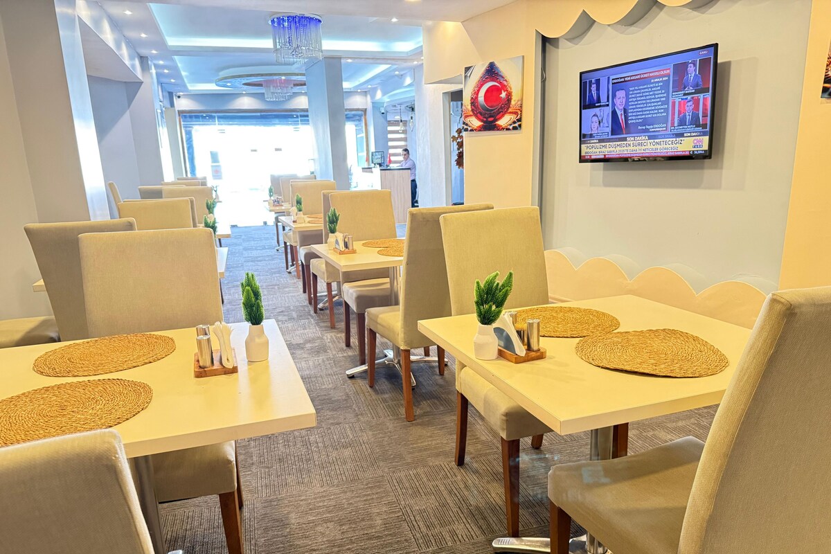 A hotel dining area with multiple tables, chairs, and a television screen displaying news.