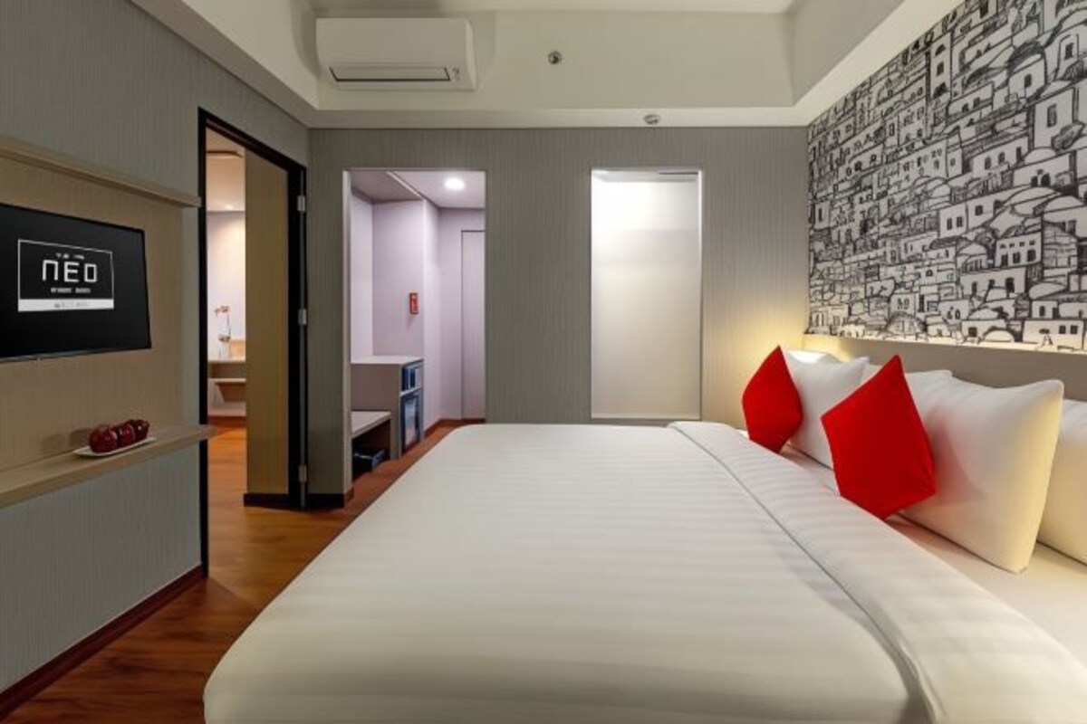 A hotel room with a large bed, a flat-screen TV on the wall, and a mural of buildings.