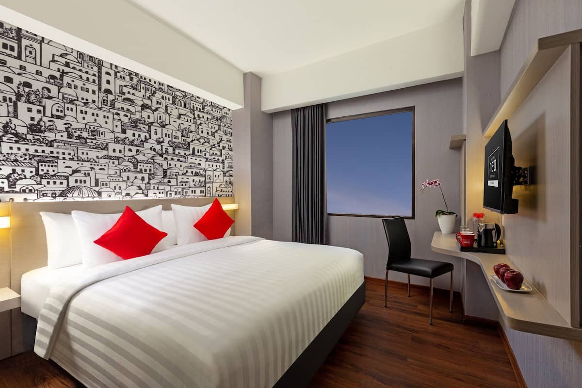 A modern hotel room with a large bed, a desk with a chair, a flat-screen TV, and a wall mural.