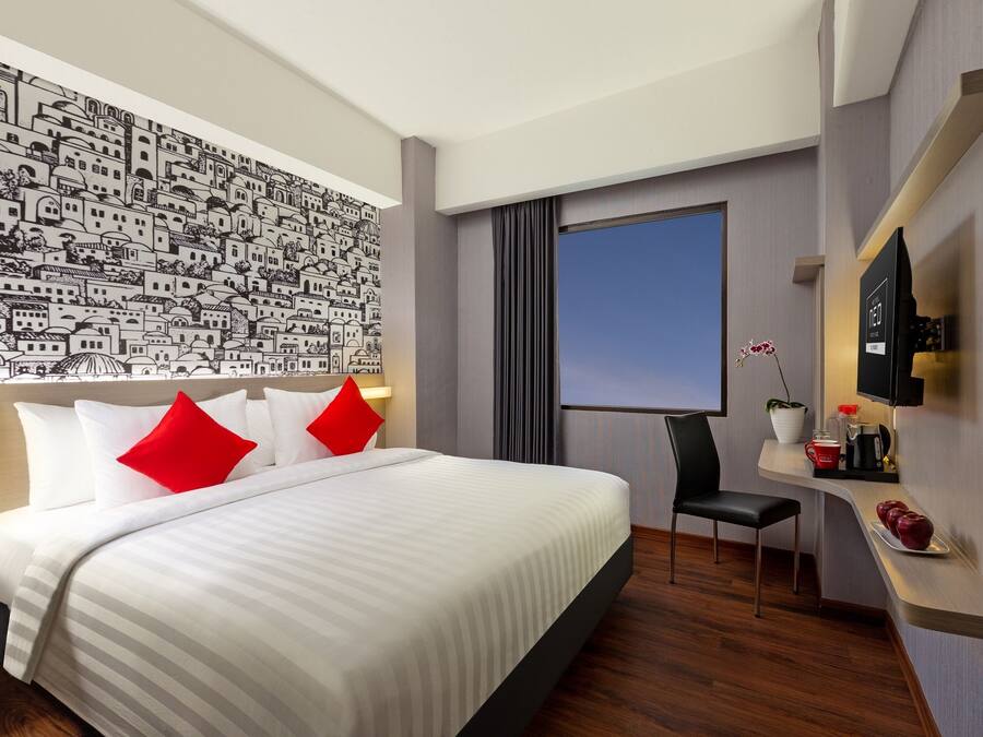 A modern hotel room with a large bed, a desk with a chair, a flat-screen TV, and a wall mural.