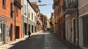 Una stretta via fiancheggiata da edifici tradizionali, con un attraversamento pedonale e linee tramviarie sopraelevate.