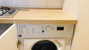 Una lavatrice compatta in una cucina con un piano di lavoro in legno e uno schienale piastrellato bianco.