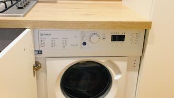 Eine kompakte Waschmaschine in einem kleinen Schrank mit Bedienfeld, einem Steckdosenanschluss darüber und einer Holz Arbeitsplatte.