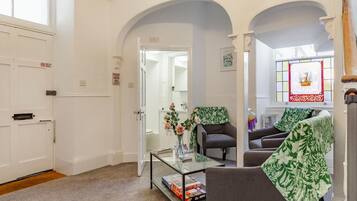 A room with a glass coffee table, two armchairs, a sofa, and a door with a sign.