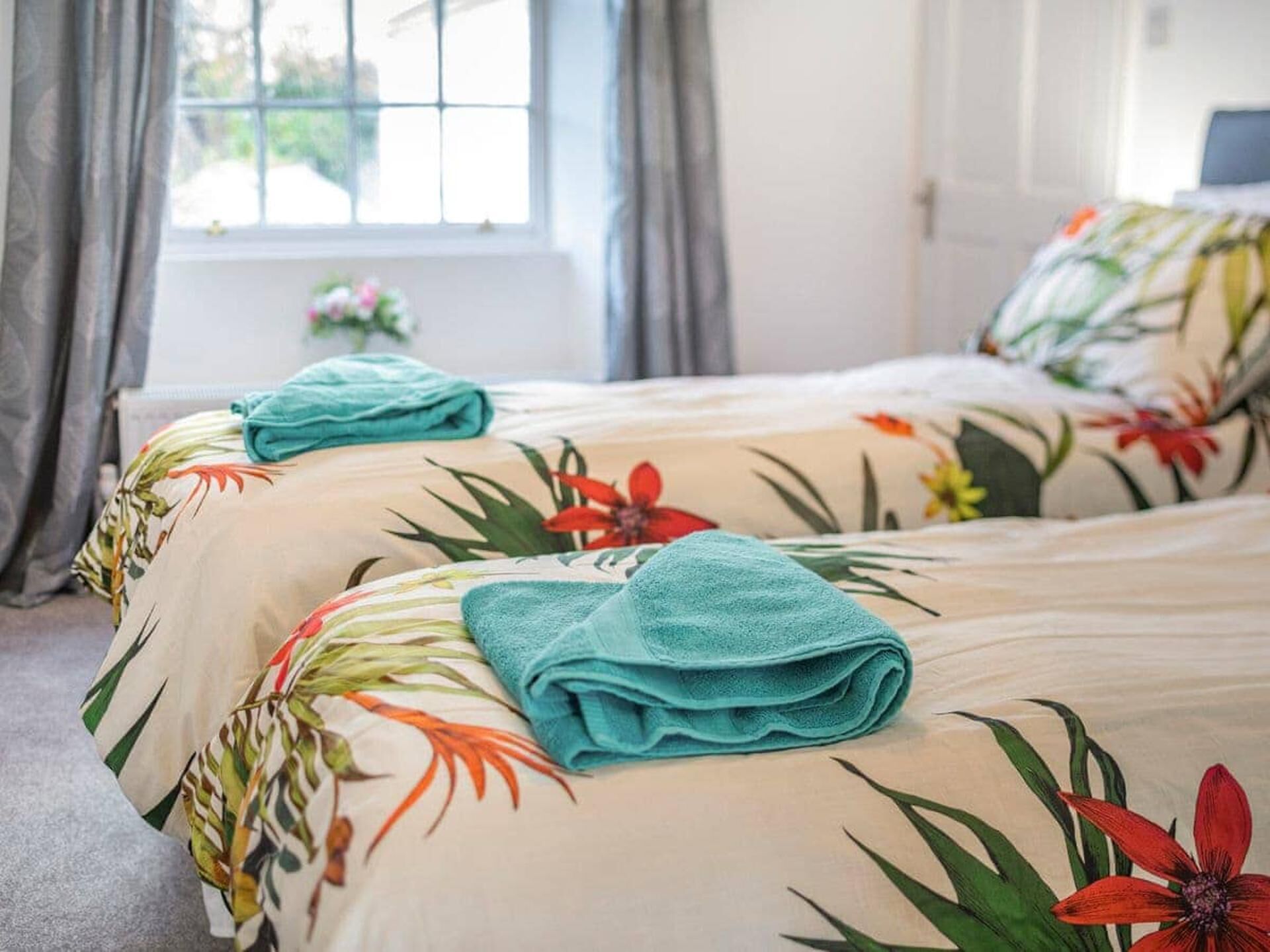 Une chambre d’hôtel avec deux lits, une literie à motifs floraux et une fenêtre avec des rideaux.