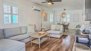 Ein modernes Wohnzimmer mit einem grauen Sofa, einem Holztisch und einem Essbereich mit Tisch und Stühlen.