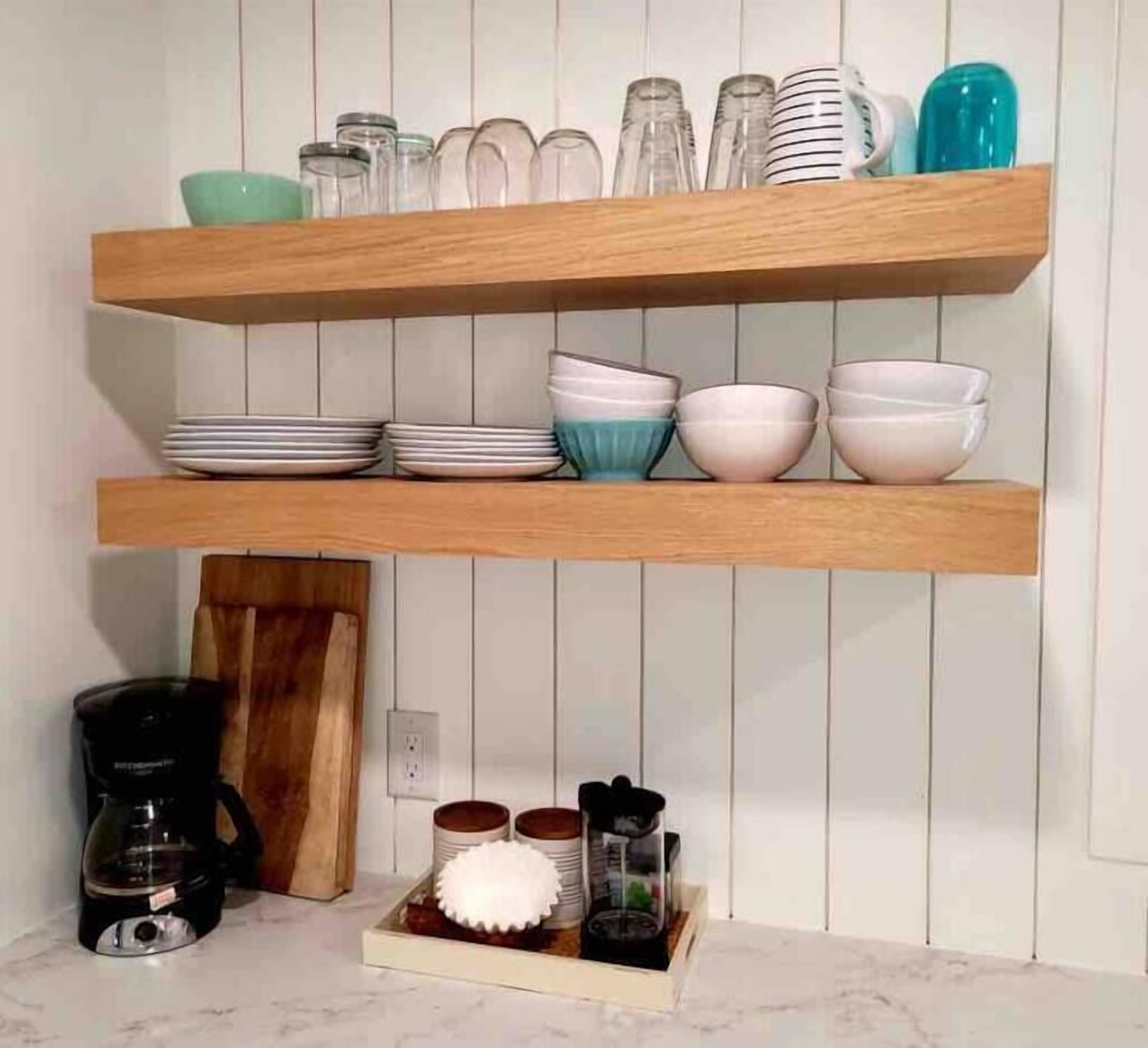 A kitchen with wooden shelves holding plates, bowls, and glassware. There is a coffee maker and a fruit bowl on the counter.