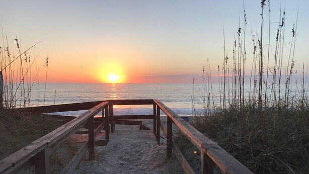 Ein hölzerner Steg führt zu einem Strand bei Sonnenuntergang.