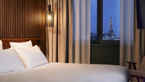 A hotel room with a bed, a nightstand, a lamp, and a view of the Eiffel Tower. - Le Bellune Paris Hotel & Spa (Paris)