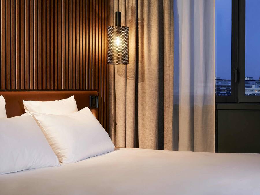 Habitación de hotel con cama, mesita de noche, lámpara y vistas a la Torre Eiffel.