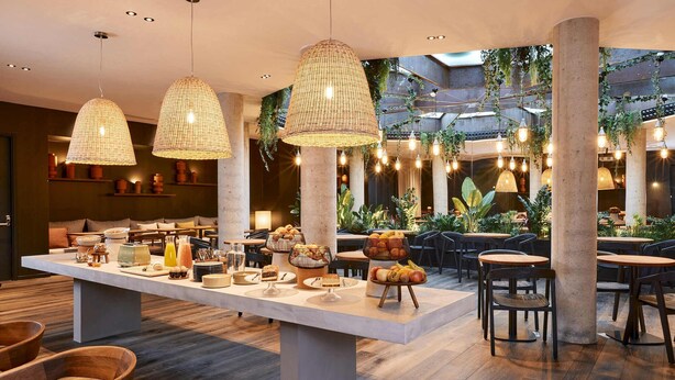 A modern dining area with a central buffet table, hanging wicker lamps, and a cozy seating arrangement. - Le Bellune Paris Hotel & Spa (Paris)