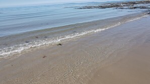 Ein Strand mit klarem Wasser, einem sandigen Ufer und fernen Felsen.