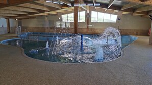 Ein Innenpool mit mehreren Wasserstrahlen und Blick ins Freie durch große Fenster.
