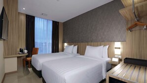 A hotel room with two beds, a desk, a chair, a TV, and a bedside table with a lamp.