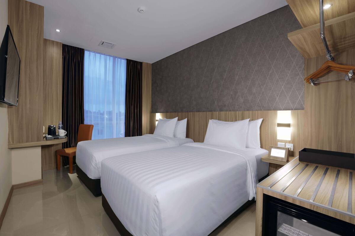 Een hotelkamer met twee bedden, een bureau, een stoel, een televisie en een nachtkastje met een lamp.