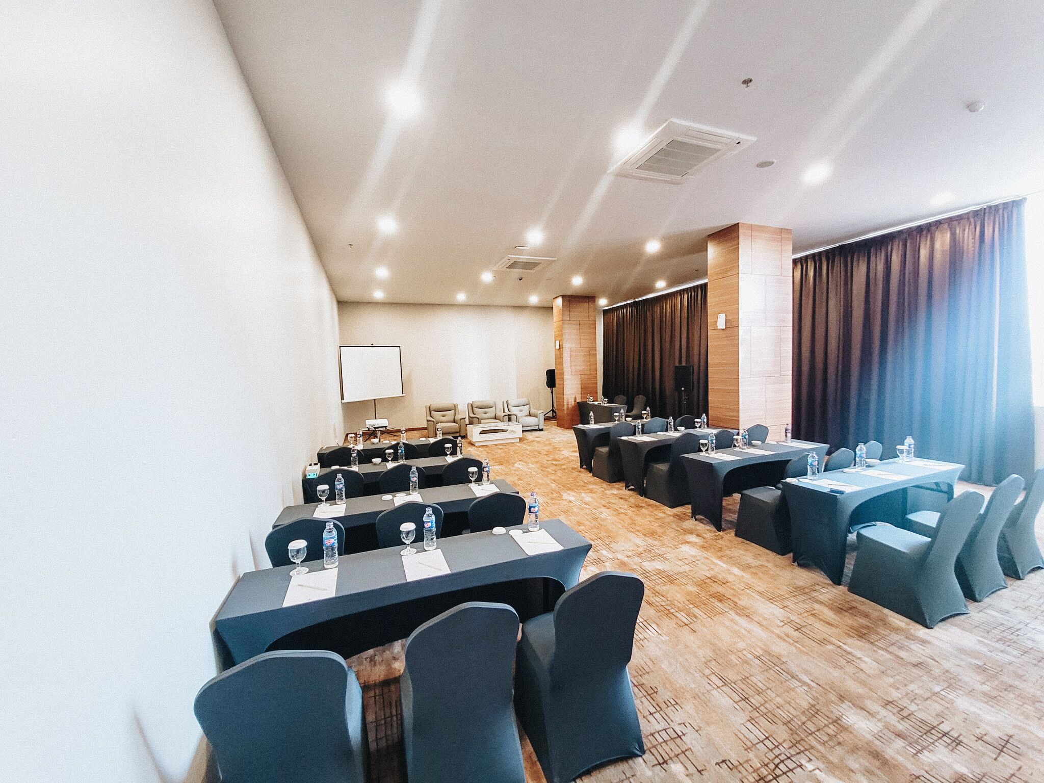 Un salón de conferencias con varias mesas y sillas, una pantalla de proyector y una zona de escenario.