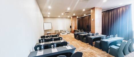 Un salón de conferencias con varias mesas y sillas, una pantalla de proyector y una zona de escenario.