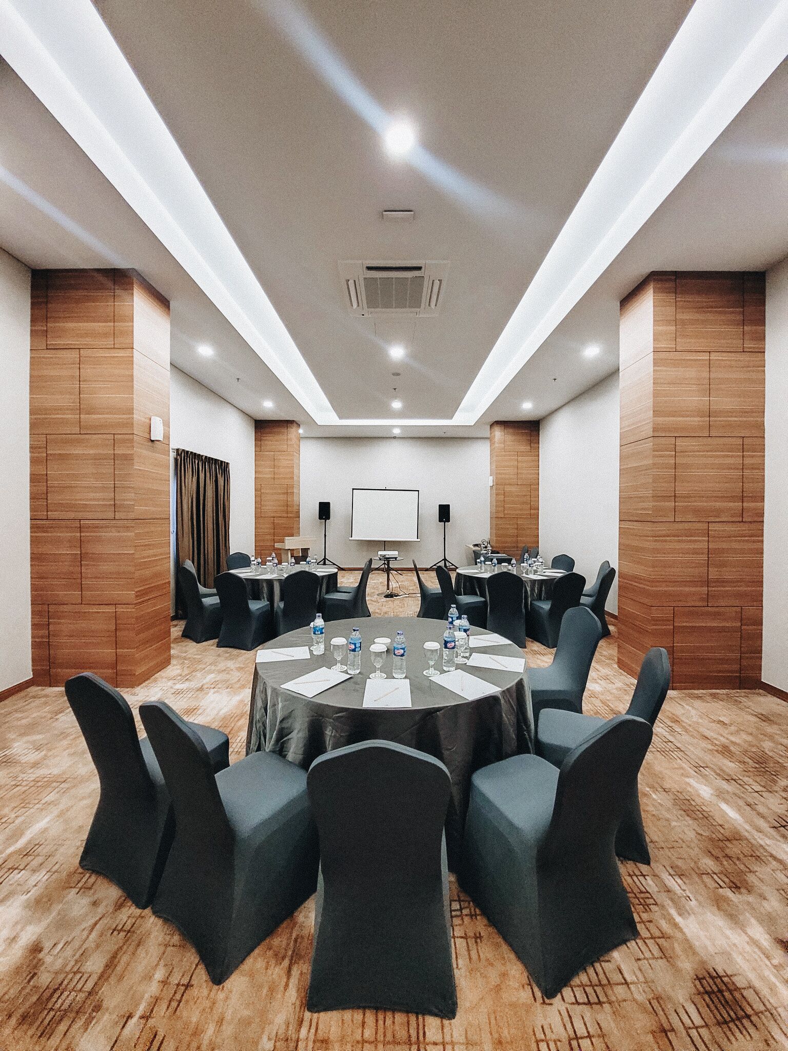 A conference room with round tables, black chairs, and a projector screen.