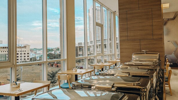 A buffet setup with multiple serving stations, large windows offering a city view, and a modern interior design.