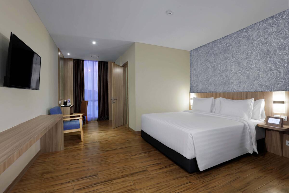 Een hotelkamer met een groot bed, een bureau, een stoel, een flatscreen televisie en een kamer met een patroon op het hoofdeinde.