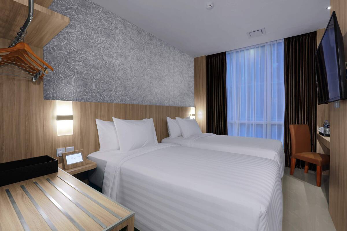 Een hotelkamer met een groot bed, een bureau, een stoel, een televisie en een raam met gordijnen.
