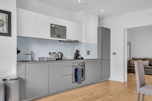 Une cuisine moderne avec des meubles gris, des appareils électroménagers en acier inoxydable et un plancher en bois.