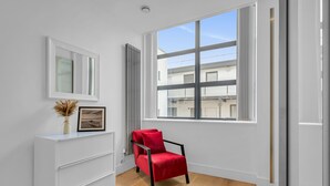 A modern room with a large window, a white cabinet, and a red chair. - Lovely 1 Bedroom Apartment in Regents Park London by MySquare (London)