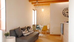 Ein gemütliches Wohnzimmer mit grauem Sofa, einem Esstisch mit Stühlen und einer Küchenzeile mit einer Uhr an der Wand.