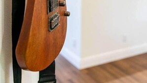 Une guitare appuyée contre un mur dans une pièce, avec un coin cuisine en arrière-plan.