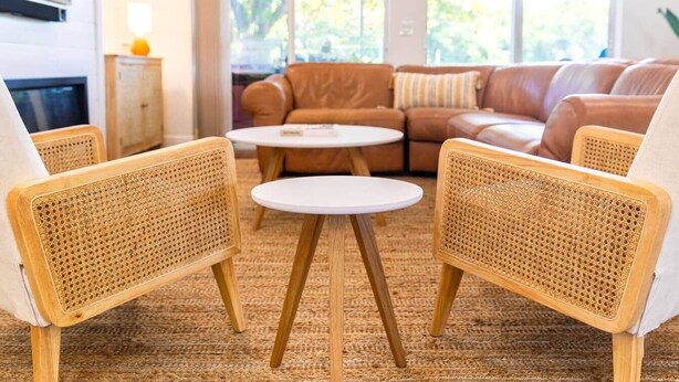 Un salon avec un canapé en cuir marron, deux fauteuils en osier et une petite table blanche.