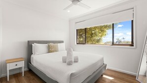 Un dormitorio con cama, mesita de noche, ventana con vista a árboles y ventilador de techo.