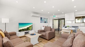 Una sala de estar moderna con televisor, sofás y un comedor con mesa y sillas.