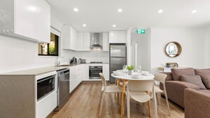 Una cocina moderna con armarios blancos, horno empotrado y un comedor con mesa y sillas redondas.