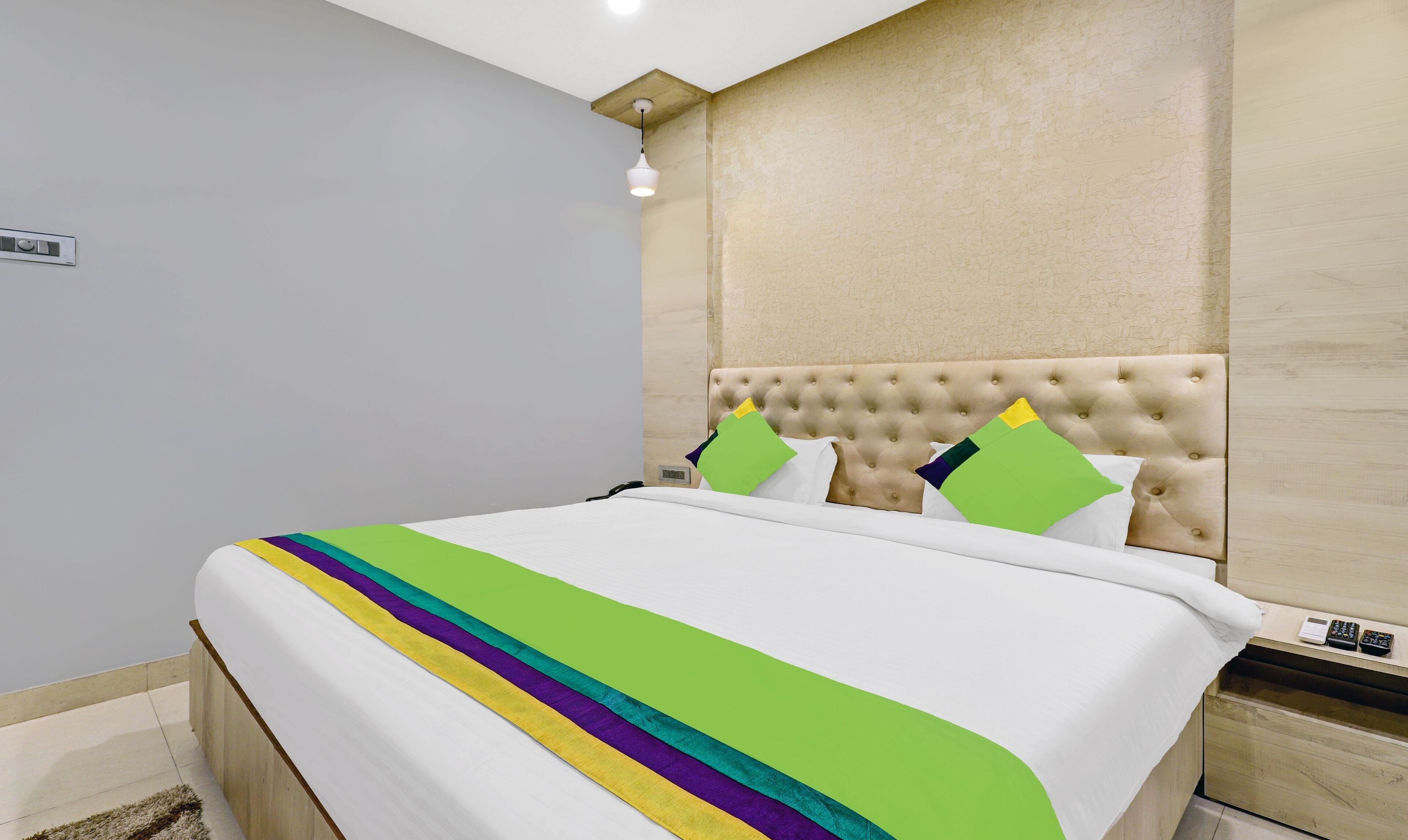 A neatly made bed with a white and green striped blanket, a tufted headboard, and a bedside table with a remote control.