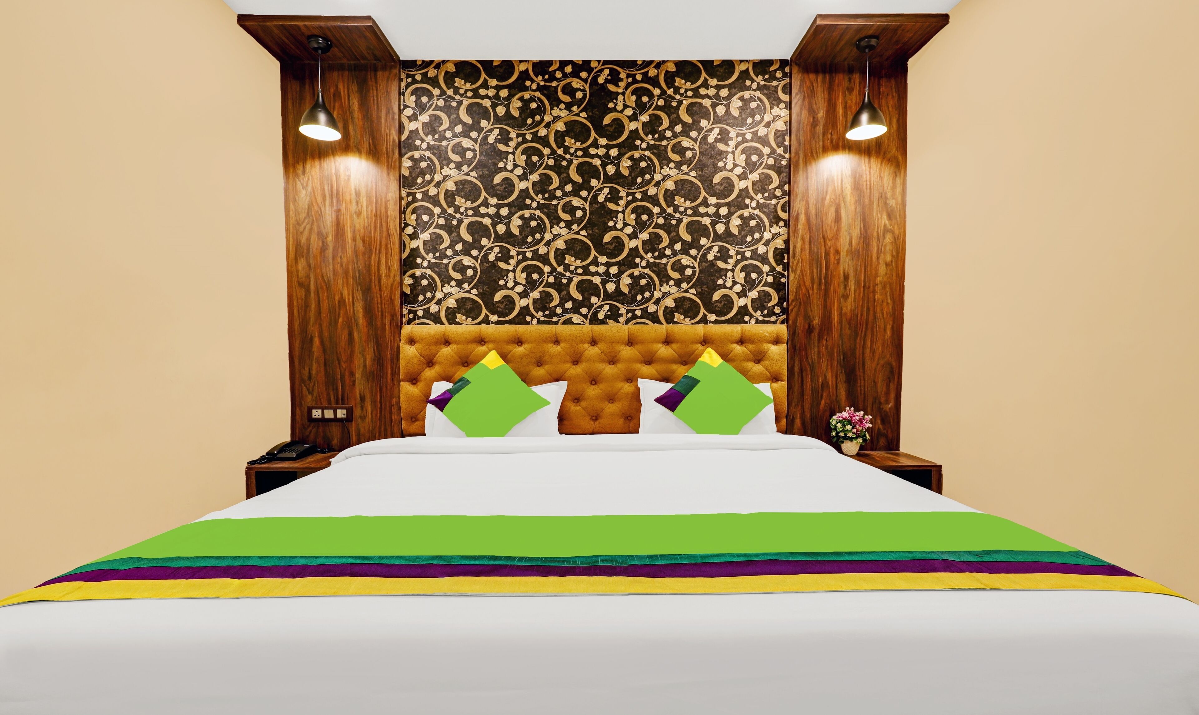 A hotel room with a tufted headboard, a patterned wallpaper, and a bed with a multicolored bedspread.