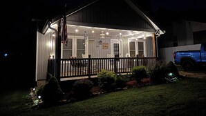A covered porch with a wooden railing, a flag, and a sign indicating the property name. - Etowah's Cottage - dog friendly, king beds, hiking, rafting, motorcycles (Etowah)