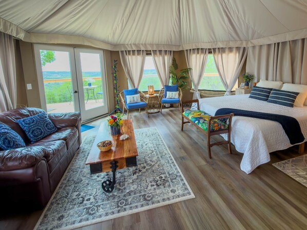 Une pi èce aménagée comme une tente, avec un lit, un canapé en cuir, une table basse en bois et une vue sur la verdure à l’extérieur.