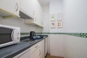 A kitchen with white cabinets, a microwave, a kettle, and a tiled backsplash.