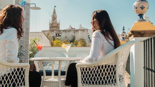 Dos personas sentadas a una mesa con una bebida, con vistas a un edificio que tiene una torre.