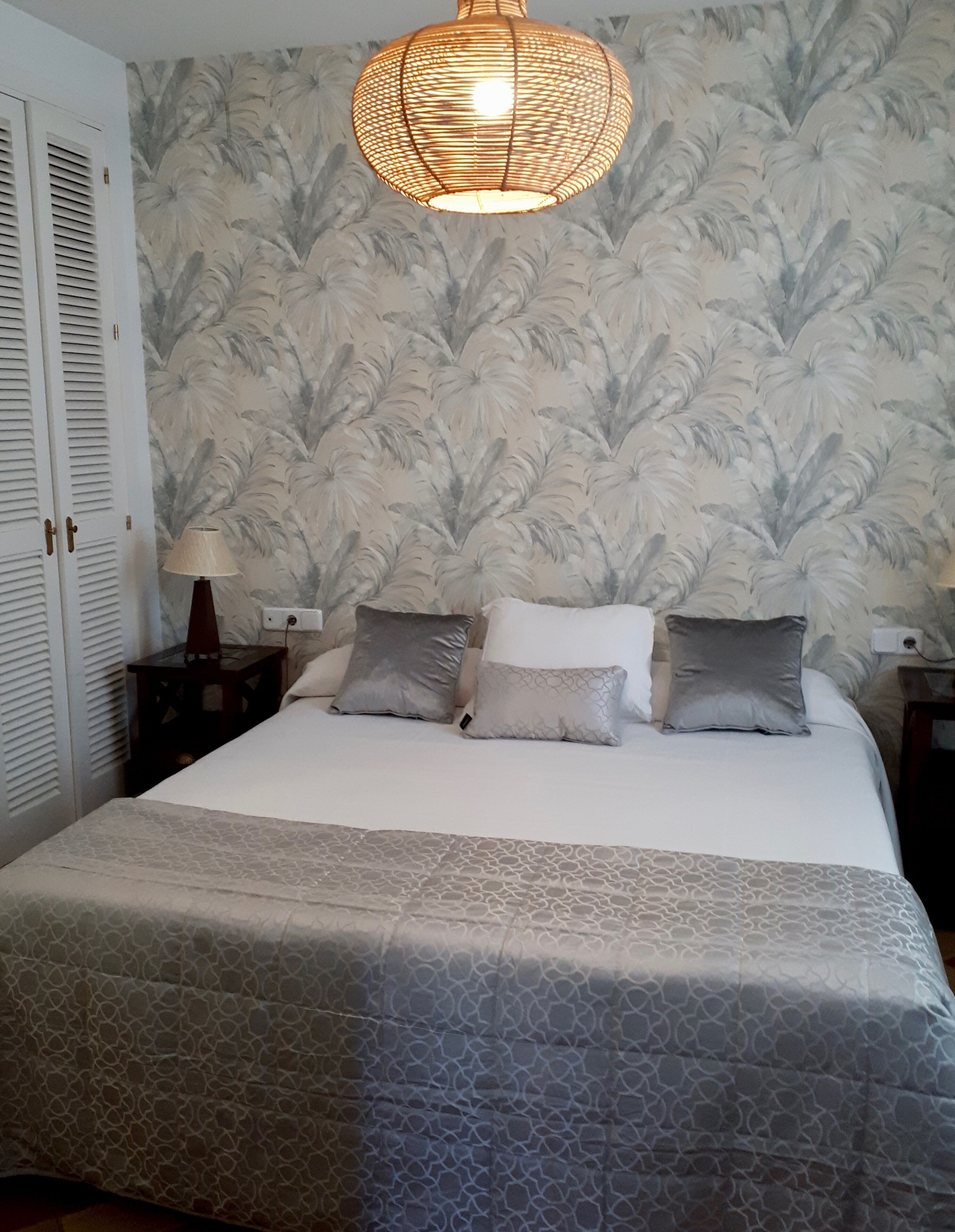 A bedroom with a bed, a nightstand, a lamp, and a wall with a leaf pattern.