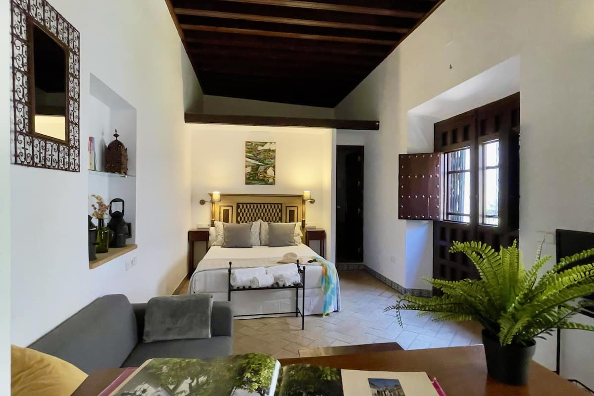 Une pièce spacieuse avec un grand lit, un plafond en bois, une plante en pot et un livre posé sur une table.